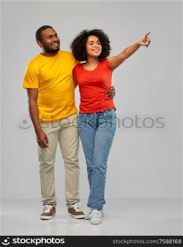 relationships and people concept - happy smiling african american couple pointing finger to something over grey background. african american couple pointing to something