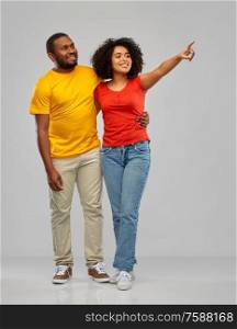relationships and people concept - happy smiling african american couple pointing finger to something over grey background. african american couple pointing to something
