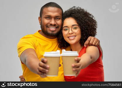 relationships and people concept - happy smiling african american couple with takeaway coffee cups over grey background. happy african american couple with coffee cups