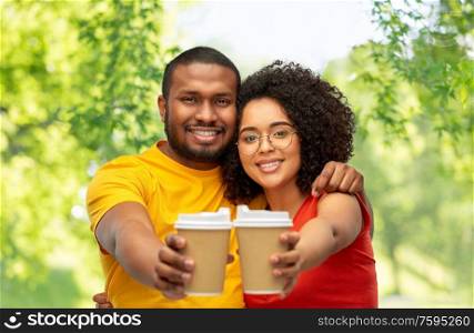 relationships and people concept - happy smiling african american couple with takeaway coffee cups over green natural background. happy african american couple with coffee cups