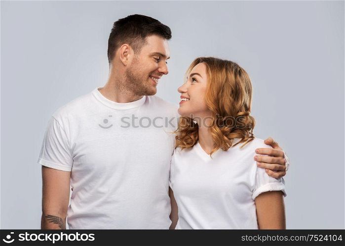 relationships and people concept - portrait of happy couple in white t-shirts looking at each other over grey background. portrait of happy couple in white t-shirts
