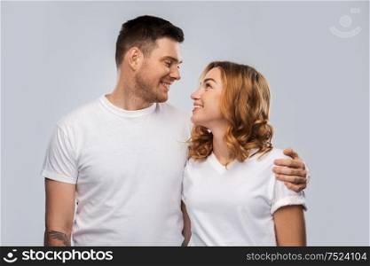 relationships and people concept - portrait of happy couple in white t-shirts looking at each other over grey background. portrait of happy couple in white t-shirts