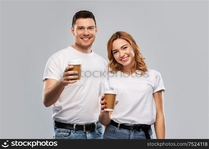 relationships and people concept - portrait of happy couple in white t-shirts with takeaway coffee cups over grey background. portrait of happy couple with takeaway coffee cups