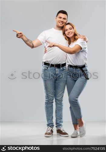 relationships and people concept - portrait of happy couple in white t-shirts showing to something over grey background. happy couple in white t-shirts pointing fingers