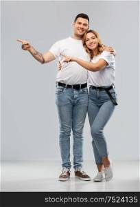 relationships and people concept - portrait of happy couple in white t-shirts showing to something over grey background. happy couple in white t-shirts pointing fingers