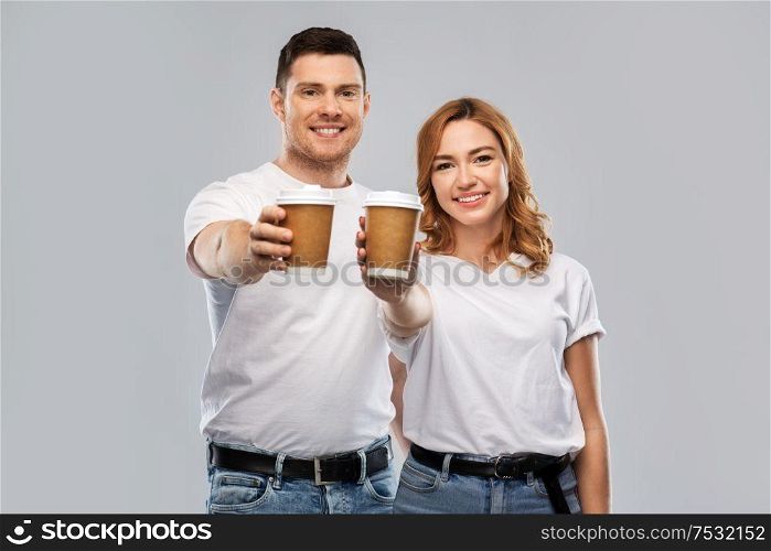 relationships and people concept - portrait of happy couple in white t-shirts with takeaway coffee cups over grey background. portrait of happy couple with takeaway coffee cups