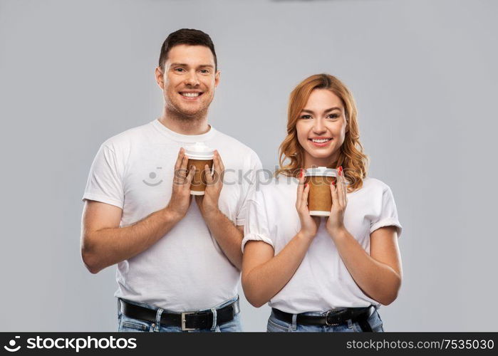 relationships and people concept - portrait of happy couple in white t-shirts with takeaway coffee cups over grey background. portrait of happy couple with takeaway coffee cups