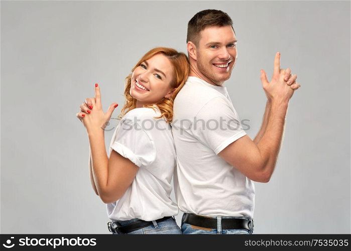 relationships and people concept - portrait of happy couple in white t-shirts making gun gesture over grey background. couple in white t-shirts shirts making gun gesture