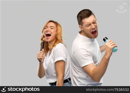 relationships and people concept - portrait of happy couple in white t-shirts couple singing to hairbrush and lotion bottle over grey background. happy couple singing to hairbrush and lotion