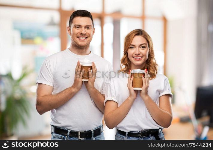 relationships and people concept - portrait of happy couple in white t-shirts with takeaway coffee cups over office background. portrait of happy couple with takeaway coffee cups