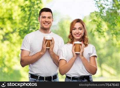 relationships and people concept - portrait of happy couple in white t-shirts with takeaway coffee cups over green natural background. portrait of happy couple with takeaway coffee cups