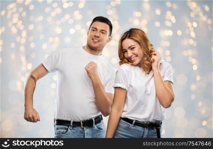 relationships and people concept - portrait of happy couple in white t-shirts dancing over holidays lights background. portrait of happy couple in white t-shirts dancing