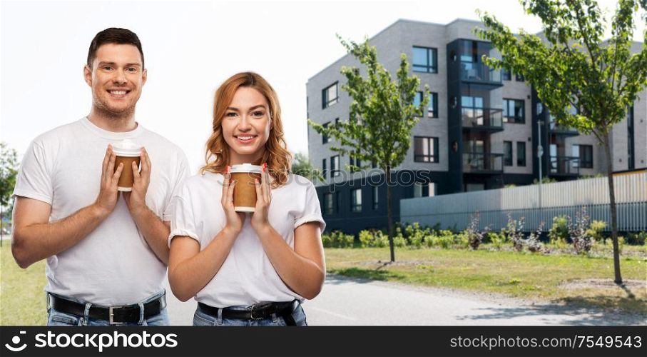 relationships and people concept - portrait of happy couple in white t-shirts with takeaway coffee cups over city street background. portrait of happy couple with takeaway coffee cups