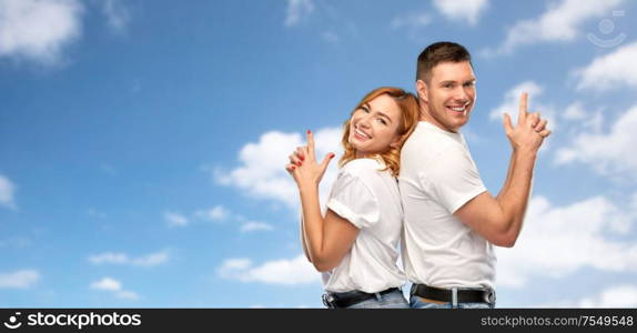 relationships and people concept - portrait of happy couple in white t-shirts making gun gesture over blue sky and clouds background. couple in white t-shirts shirts making gun gesture