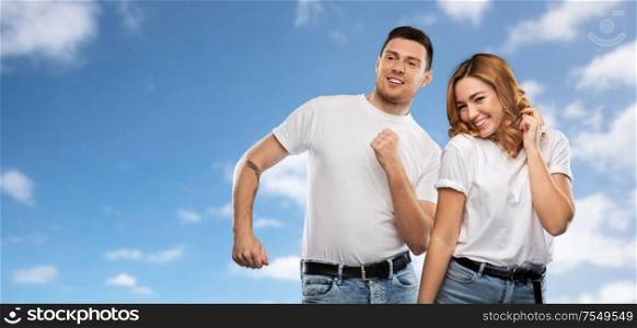 relationships and people concept - portrait of happy couple in white t-shirts dancing over blue sky and clouds background. portrait of happy couple in white t-shirts dancing