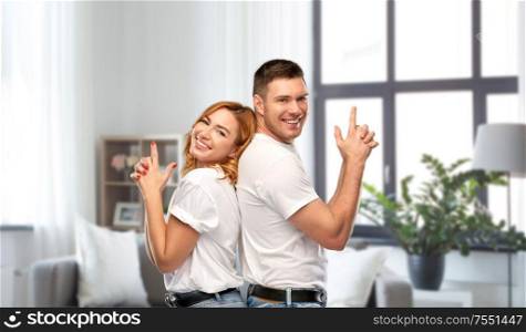 relationships and people concept - portrait of happy couple in white t-shirts making gun gesture over home background. couple in white t-shirts shirts making gun gesture