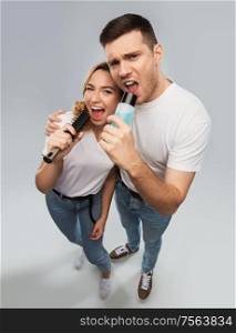 relationships and people concept - portrait of happy couple in white t-shirts couple singing to hairbrush and lotion bottle over grey background. happy couple singing to hairbrush and lotion