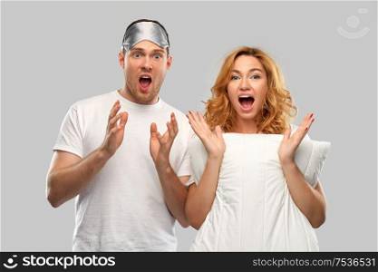 relationships and people concept - scared couple in white t-shirts with eye sleeping mask and pillow over grey background. scared couple with eye sleeping mask and pillow