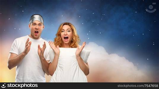 relationships and people concept - scared couple in white t-shirts with eye sleeping mask and pillow over starry night sky background. couple with eye sleeping mask and pillow at night
