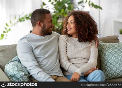 relationships, communication and people concept - happy african american couple sitting on sofa and talking at home. african american couple on sofa talking at home