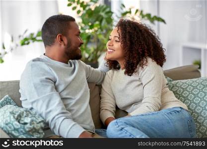 relationships, communication and people concept - happy african american couple sitting on sofa and talking at home. african american couple on sofa talking at home
