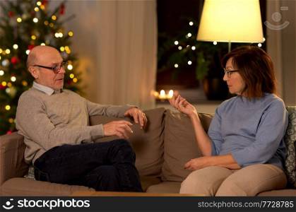 relationships difficulties, communication and people concept - unhappy senior couple arguing or discussing problem at home over christmas tree lights on background. unhappy senior couple arguing at home on christmas