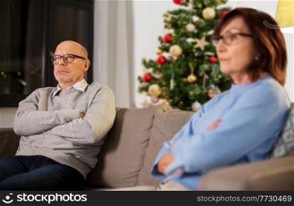 relationships difficulties, winter holidays and people concept - unhappy senior couple sitting on sofa at home over christmas tree on background. unhappy senior couple at home on christmas