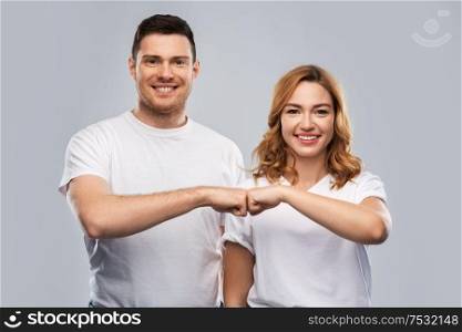 relationships, friendship and people concept - portrait of happy couple in white t-shirts making fist bump gesture over grey background. portrait of happy couple in white t-shirts