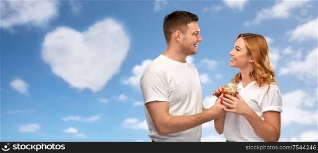 relationships, holiday and valentine&rsquo;s day concept - happy couple in white t-shirts with gift over blue sky and heart shaped cloud background. happy couple in white t-shirts with gift
