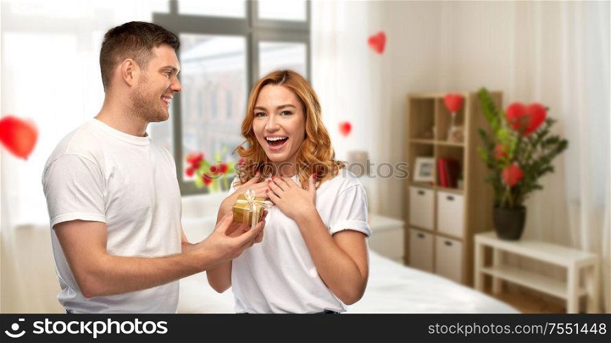 relationships, holiday and valentine&rsquo;s day concept - happy couple in white t-shirts with christmas gift over home bedroom decorated with heart shaped balloons background. happy couple with gift at home