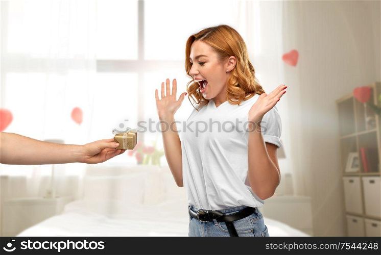 relationships, holiday and valentine&rsquo;s day concept - happy woman in white t-shirt receiving little gift box from man over bedroom decorated with heart shaped balloons background. happy couple with gift on valentines day at home