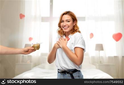 relationships, holiday and valentine&rsquo;s day concept -happy woman in white t-shirt receiving little gift box from man over bedroom decorated with heart shaped balloons background. happy couple in white t-shirts with christmas gift