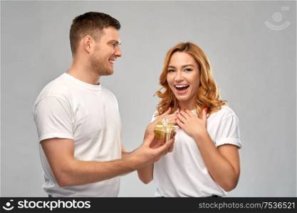 relationships, holiday and valentines day concept - happy couple in white t-shirts with christmas gift over grey background. happy couple in white t-shirts with christmas gift