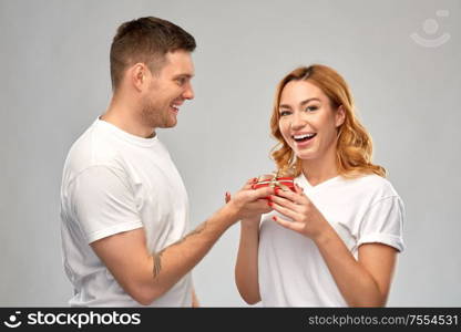 relationships, holiday and valentines day concept - happy couple in white t-shirts with christmas gift over grey background. happy couple in white t-shirts with christmas gift