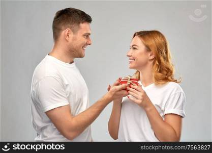 relationships, holiday and valentines day concept - happy couple in white t-shirts with christmas gift over grey background. happy couple in white t-shirts with christmas gift