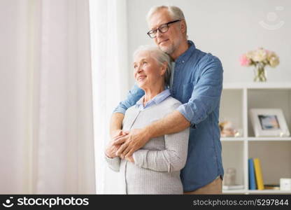 relationships, old age and people concept - happy senior couple looking through window and hugging at home. happy senior couple looking through window at home