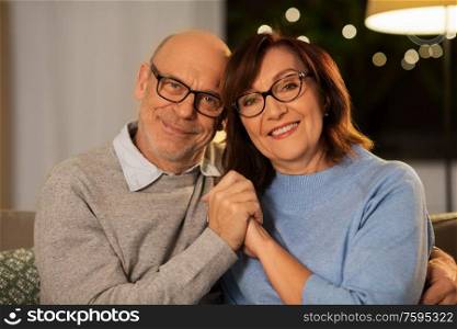 relationships, old age and people concept - happy smiling senior couple hugging on sofa at home in evening. happy senior couple hugging on sofa at home