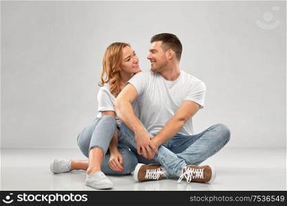 relationships, style and people concept - happy couple in white t-shirts sitting on floor over grey background. happy couple in white t-shirts sitting on floor