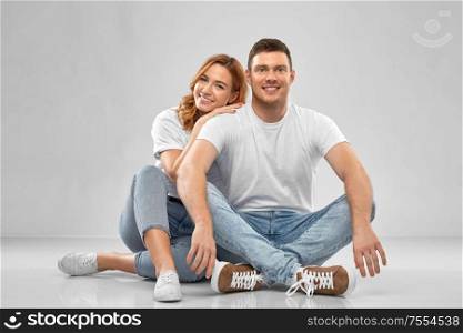 relationships, style and people concept - happy couple in white t-shirts sitting on floor over grey background. happy couple in white t-shirts sitting on floor