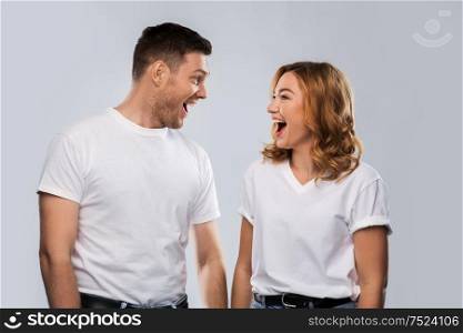 relationships, style and people concept - portrait of happy couple in white t-shirts looking at each and laughing other over grey background. portrait of laughinh couple in white t-shirts