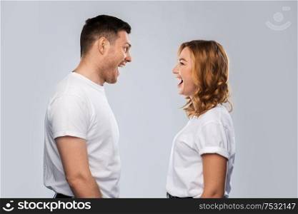 relationships, style and people concept - portrait of happy couple in white t-shirts looking at each and laughing other over grey background. portrait of laughinh couple in white t-shirts