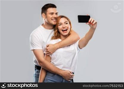 relationships, technology and people concept - happy couple in white t-shirts taking selfie smartphone by over grey background. happy couple in white t-shirts taking selfie