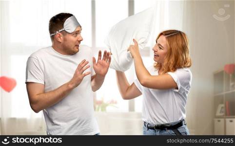 relationships, valentine&rsquo;s day and people concept - couple in white t-shirts with eye sleeping mask having pillow fight over home room decorated with heart shaped balloons background. couple with eye sleeping mask having pillow fight