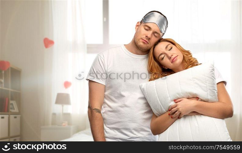 relationships, valentine&rsquo;s day and people concept - couple in white t-shirts with eye sleeping mask and pillow over home bedroom decorated with heart shaped balloons background. couple with eye sleeping mask and pillow at home
