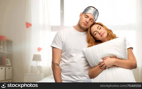 relationships, valentine&rsquo;s day and people concept - couple in white t-shirts with eye sleeping mask and pillow over home bedroom decorated with heart shaped balloons background. couple with eye sleeping mask and pillow at home