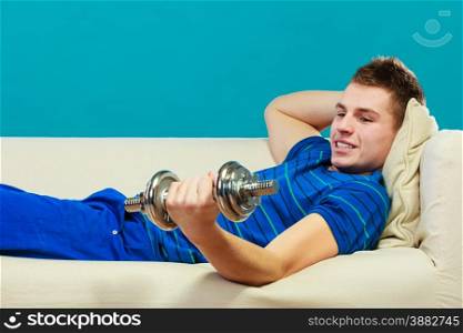 Relax after sport activity. Young man fit body relaxing on couch or having dreams of muscular body, dumb bell in hand