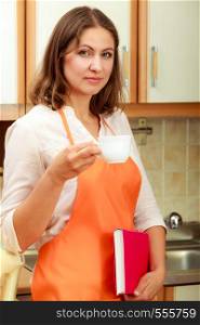 Relax and rest in kitchen. Middle aged woman chef housekeeper holding cookbook with cup of tea coffee. Housewife resting at home.. Female cook relaxing in kitchen.
