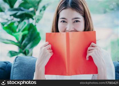 Relax asian woman reading book sitting on sofa in living room holding book to read. Young woman relaxation reader reading open book leisure mind. Happiness beauty woman person smiling face happy time