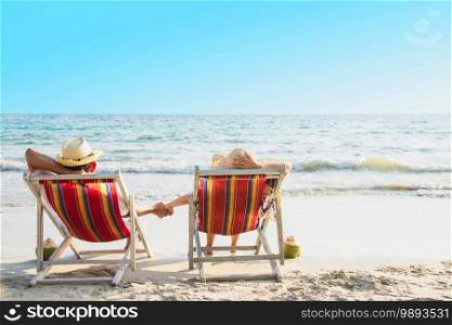 Relax couple lay down on beach chair with sea wave background - man and woman have vacation at sea nature concept. Relax couple lay down on beach chair with sea wave background