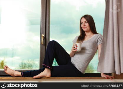 Relax indoors casual concept. Young girl in morning. Cheerful lady sitting on terrace next to window drinking coffee from cup enjoying breakfast.. Young girl in morning.